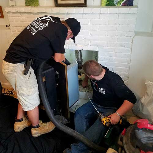 Two techs cleaning chimney both with logo t-shirts brick surround is white