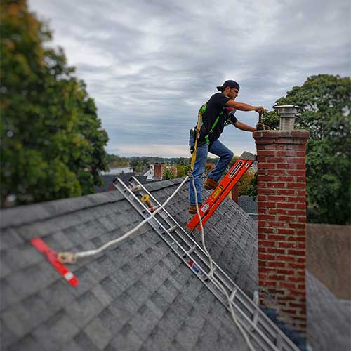 Tech cleaning chimney on the roof with safety equipment and two ladders
