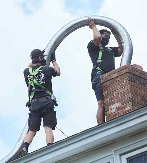 Two techs lining a chimney on top of house with safety equipment