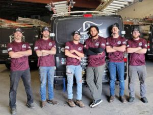 Team Photo - six guys standing in warehouse in front of three company vans